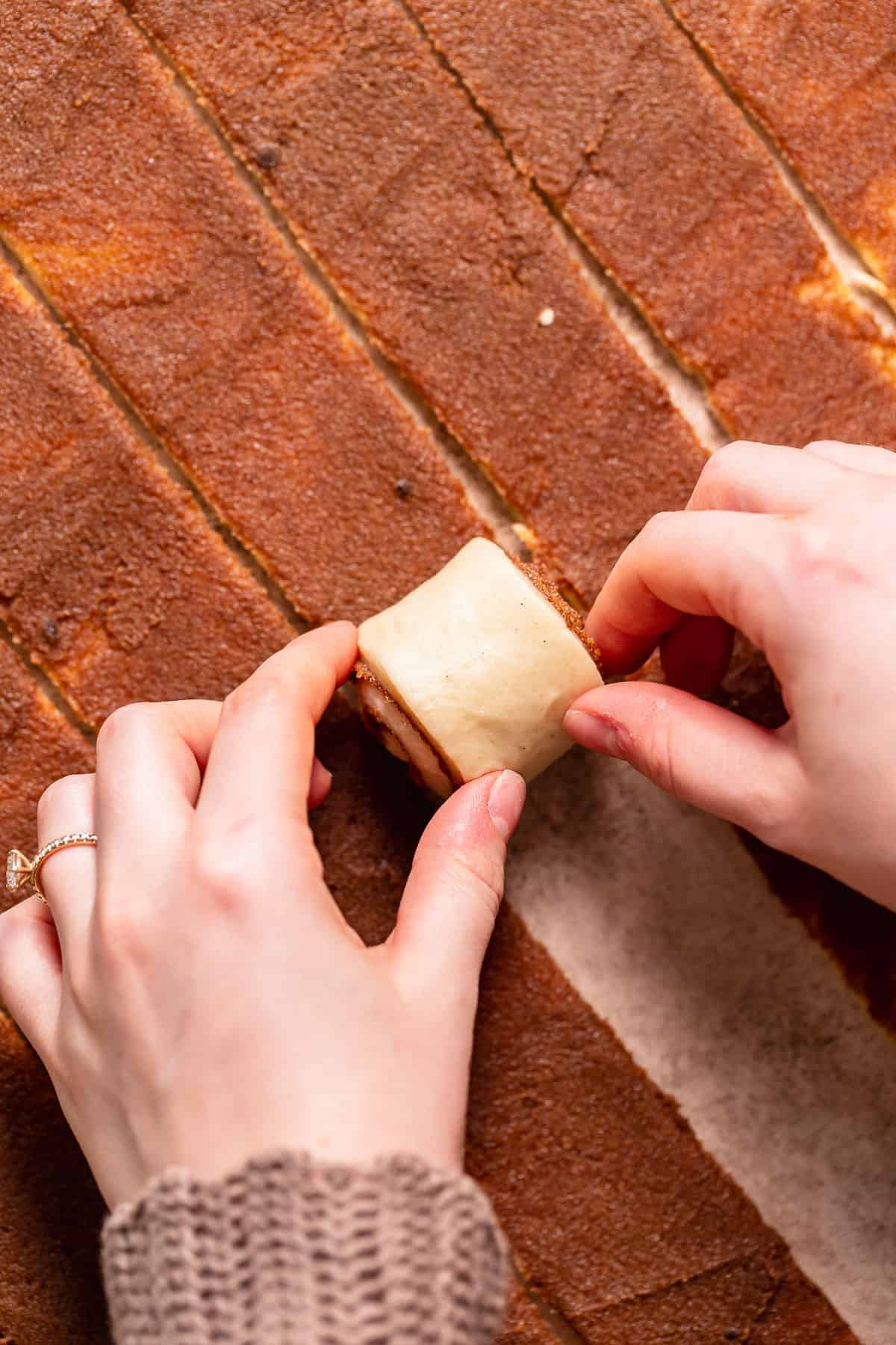 Two hands rolling up the cinnamon dough into rolls.