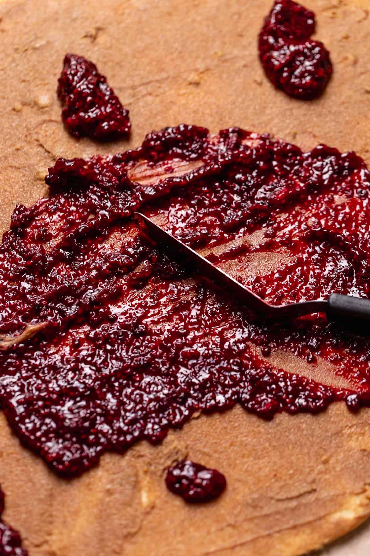 A spatula spreading the berry jam across the cinnamon sugar filling.