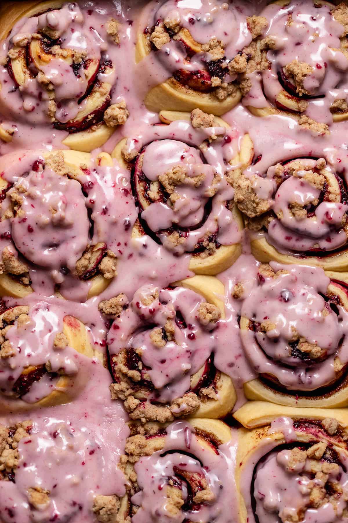 Blackberry cinnamon rolls with berry icing in a baking pan.