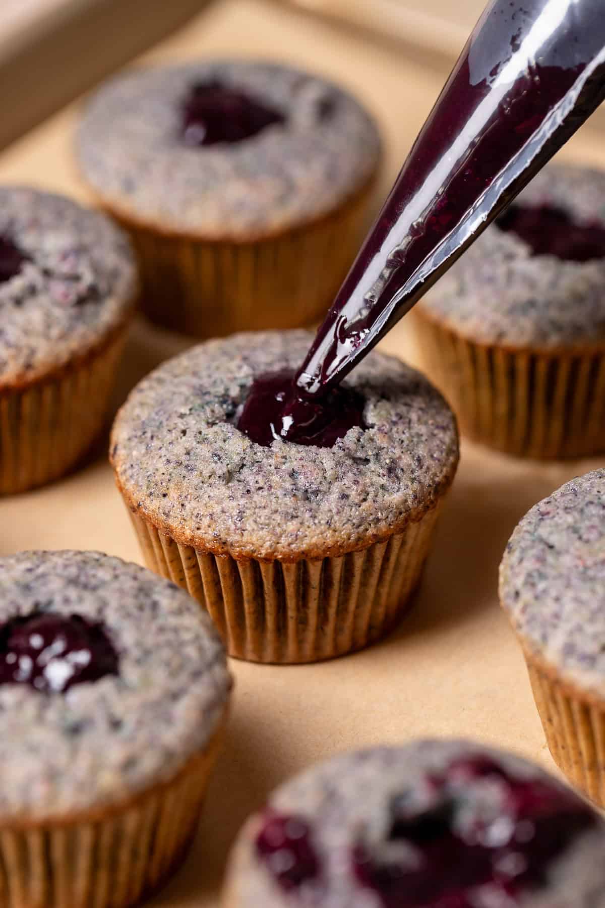 A piping bag filling the center of a cupcake with blueberry filling.