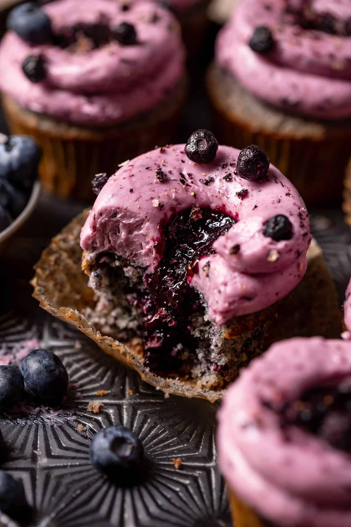 A blueberry cupcake with a bite out of it showing the gooey blueberry filled center.