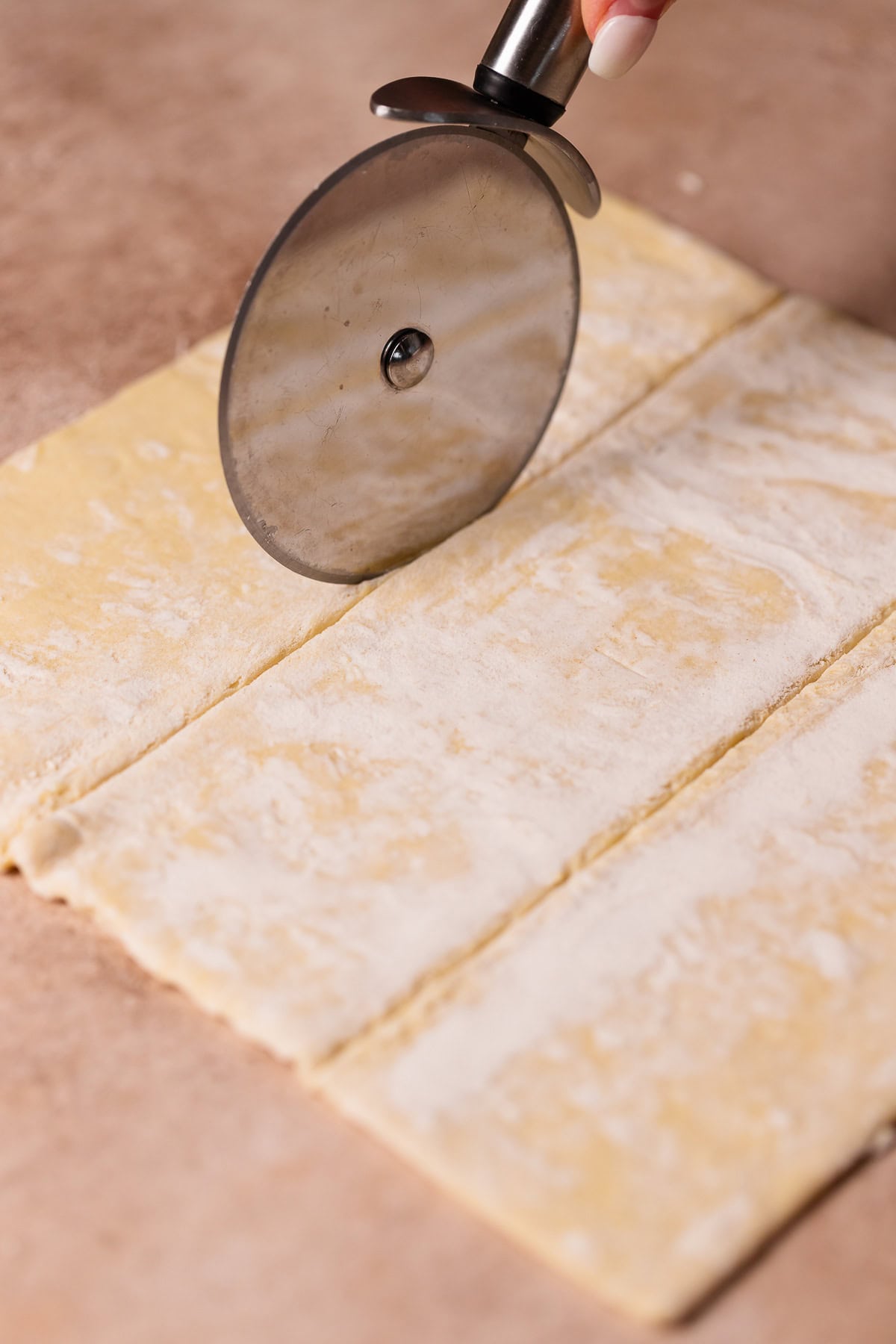 A pizza wheel cutting out squares of puff pastry.