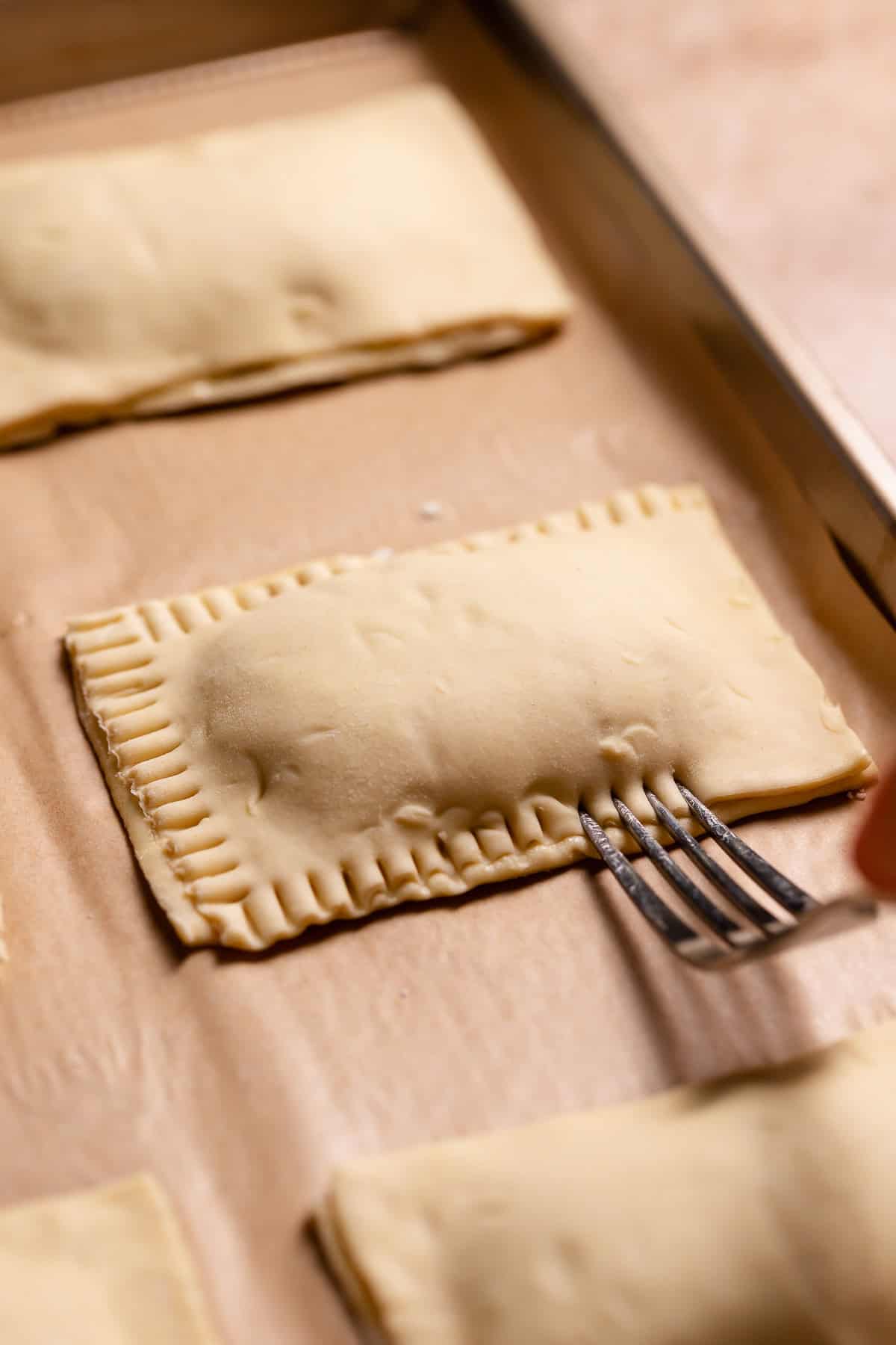 A fork crimping the edges of the filled pastries.