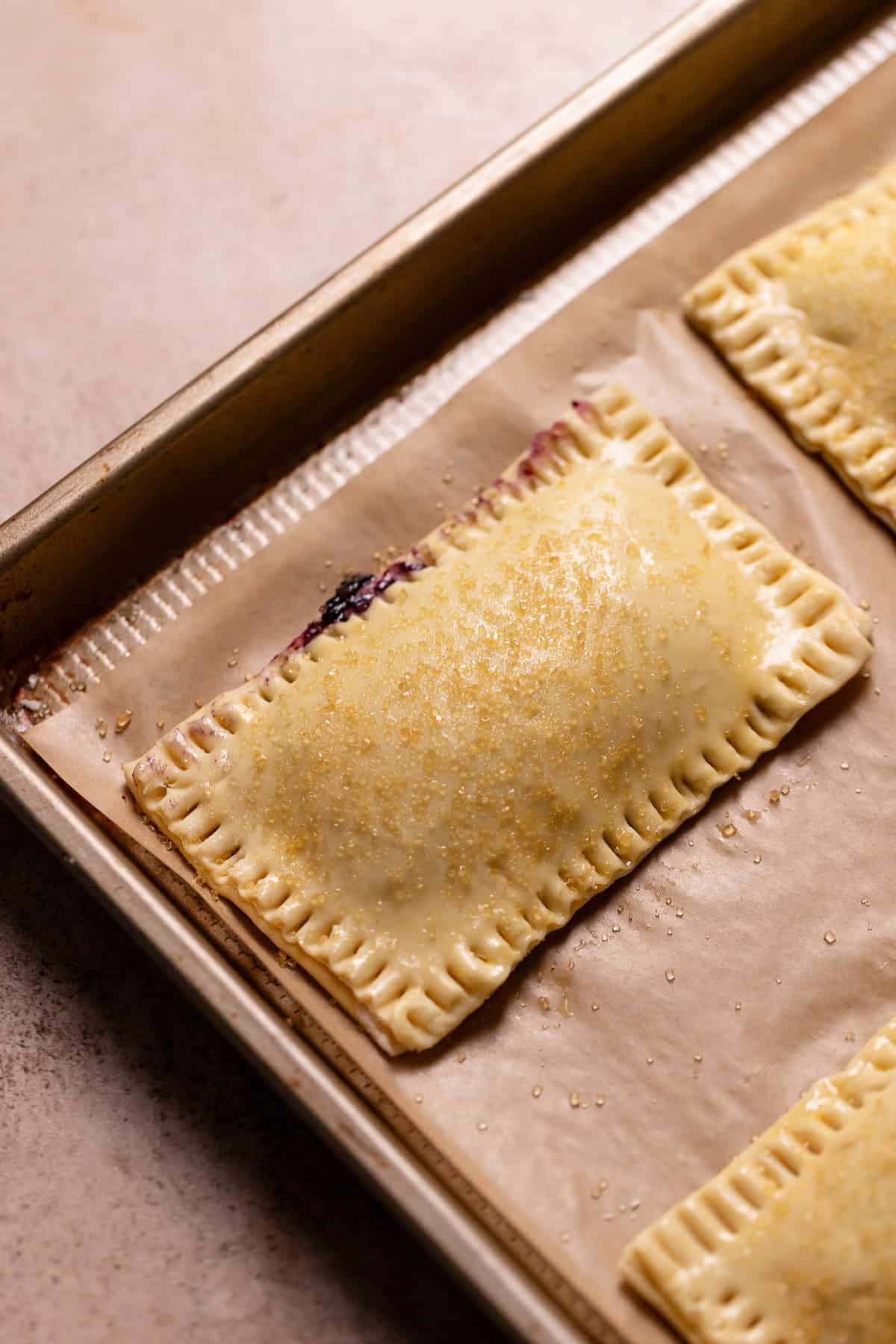 Filled toaster pastries on a baking sheet covered in turbinado sugar before baking.