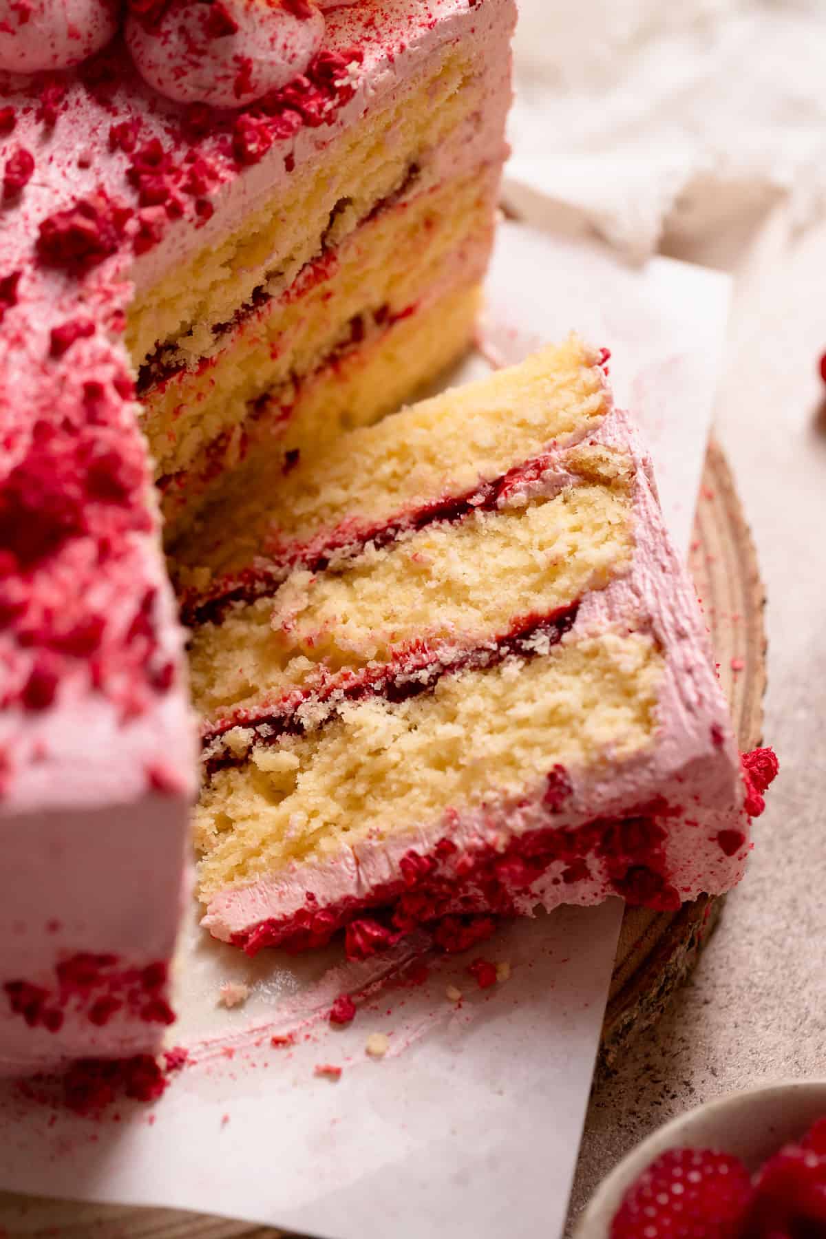 A slice of lemon raspberry cake on a wooden cake stand.