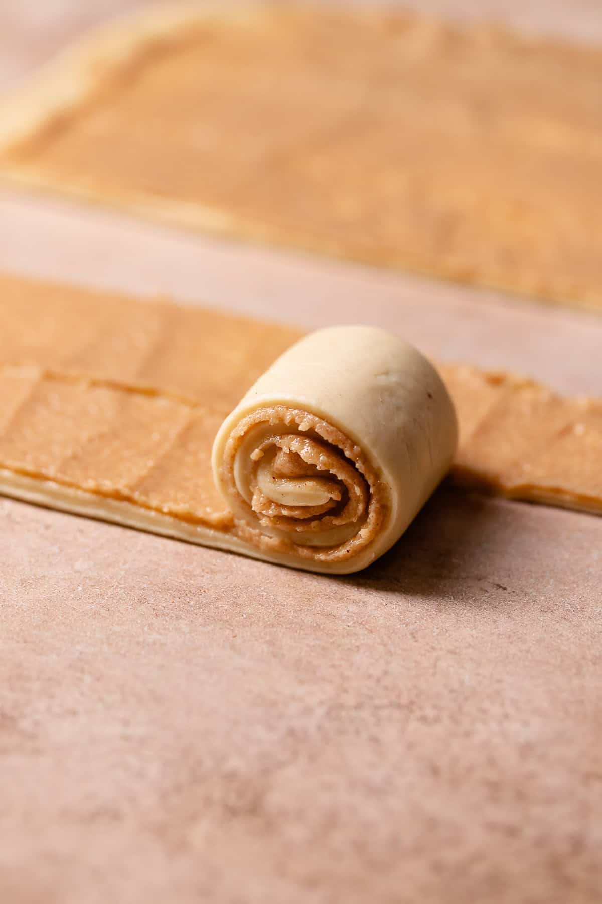 A strip of cinnamon roll dough being rolled up into a bun.