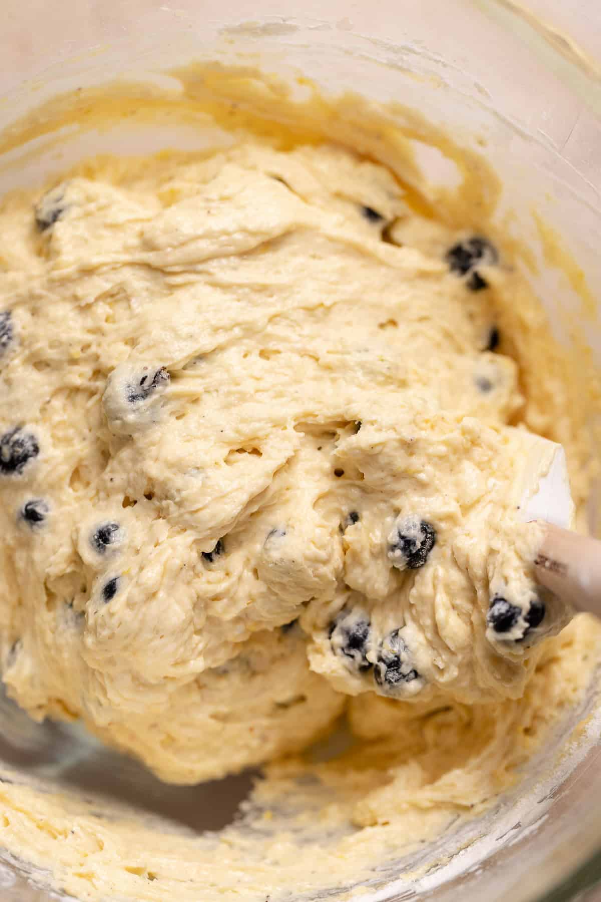 A spatula folding the fresh blueberries into the cake batter.