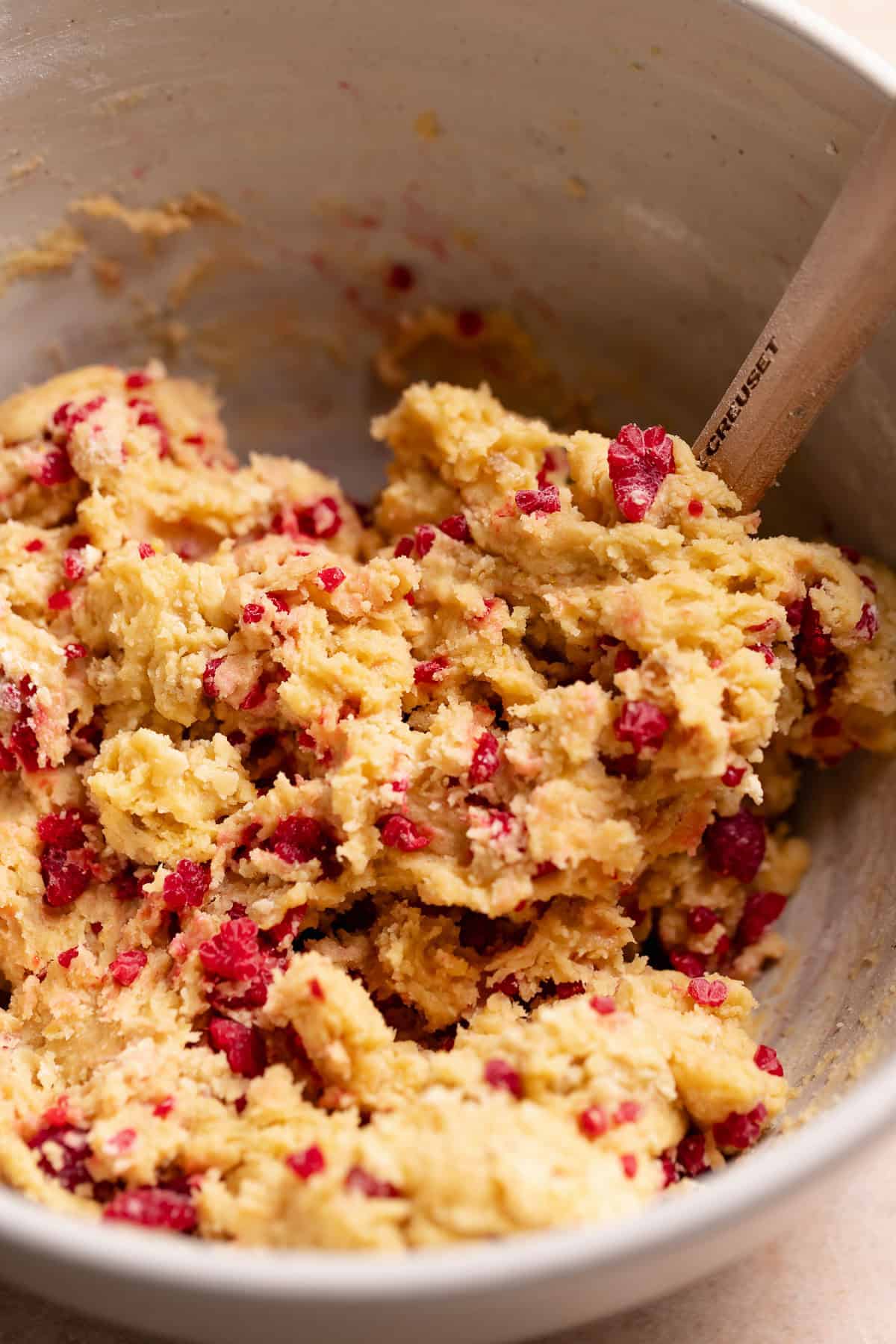 Lemon cookie dough with frozen raspberry bits being folded in.