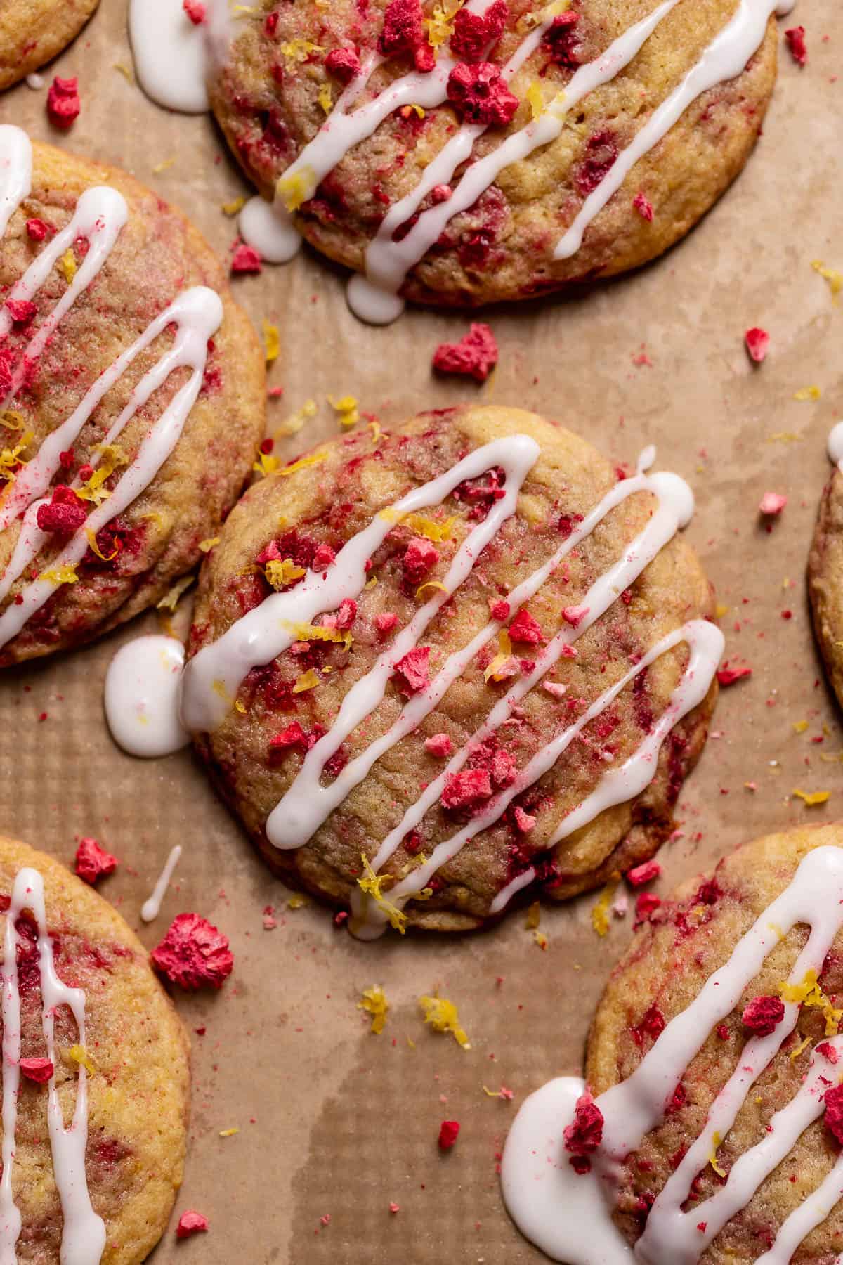 Cookies on a baking sheet drizzled with lemon glaze and sprinkled with raspberries and lemon zest.