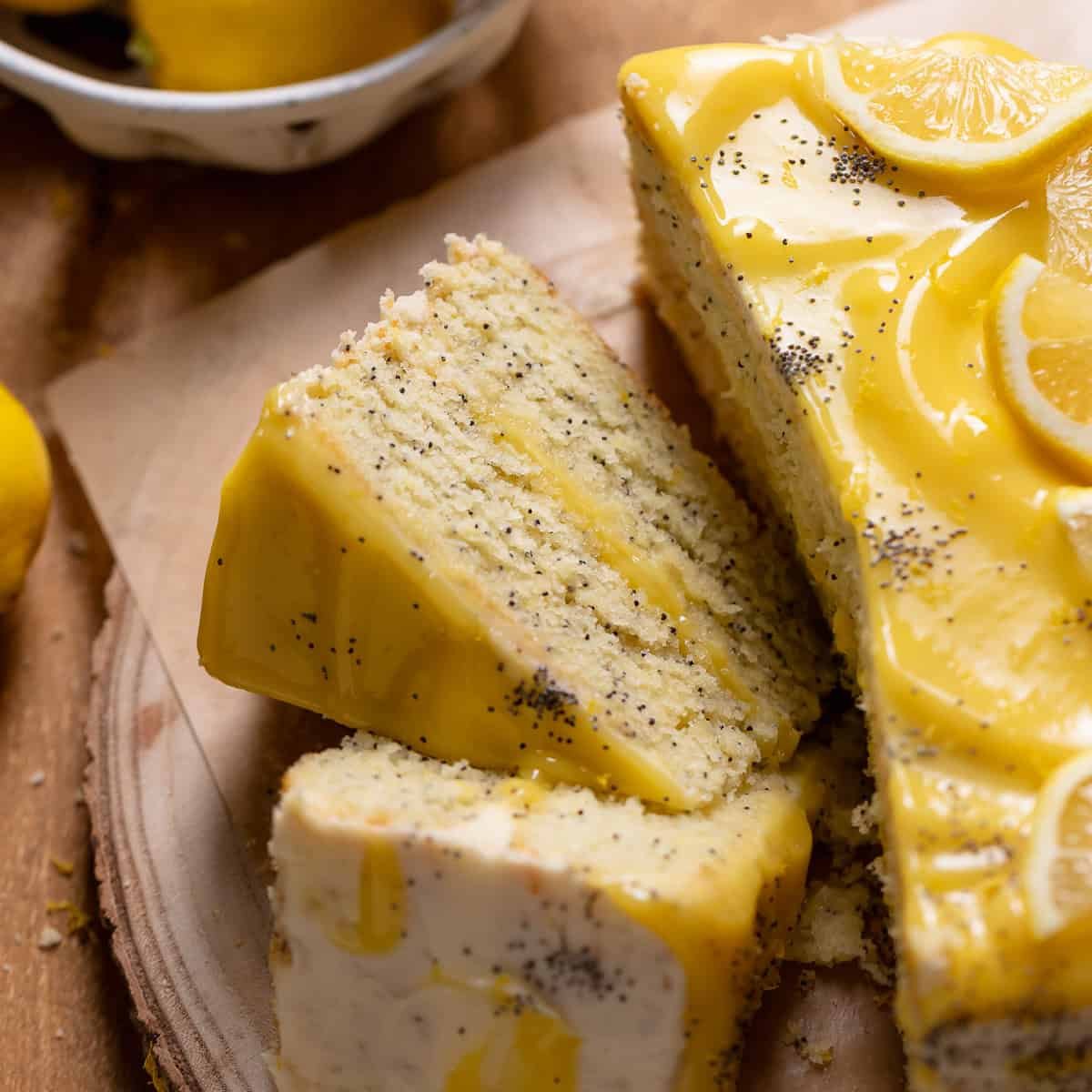 Lemon poppy seed layer cake cut into slices on a wooden platter.