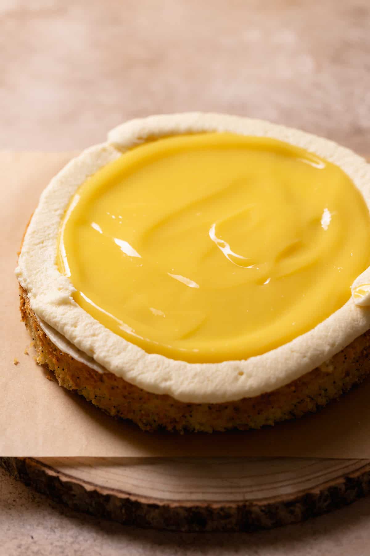 A layer of lemon cake on a platter with cream cheese frosting border and lemon curd center.