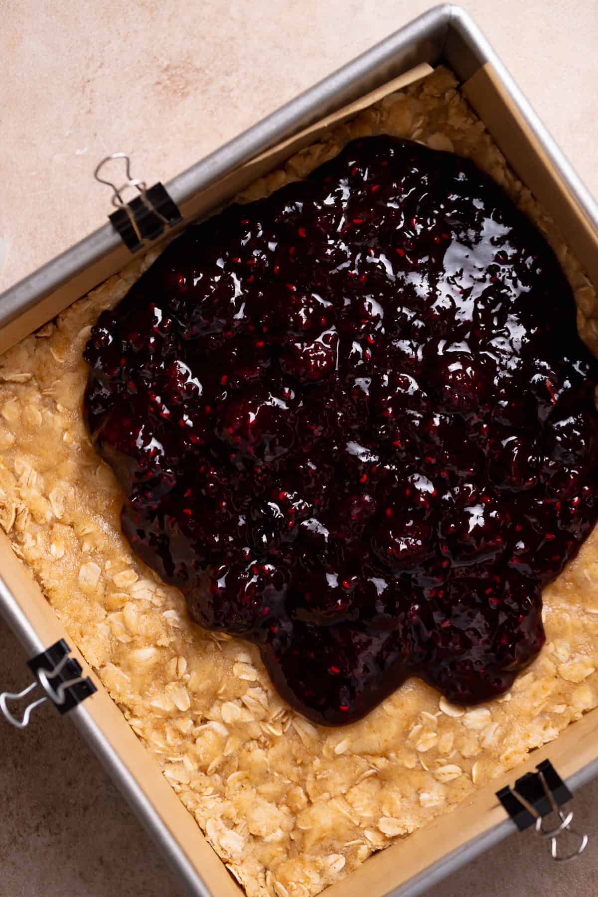Mixed berry jam being spread over the oat crumble dough.