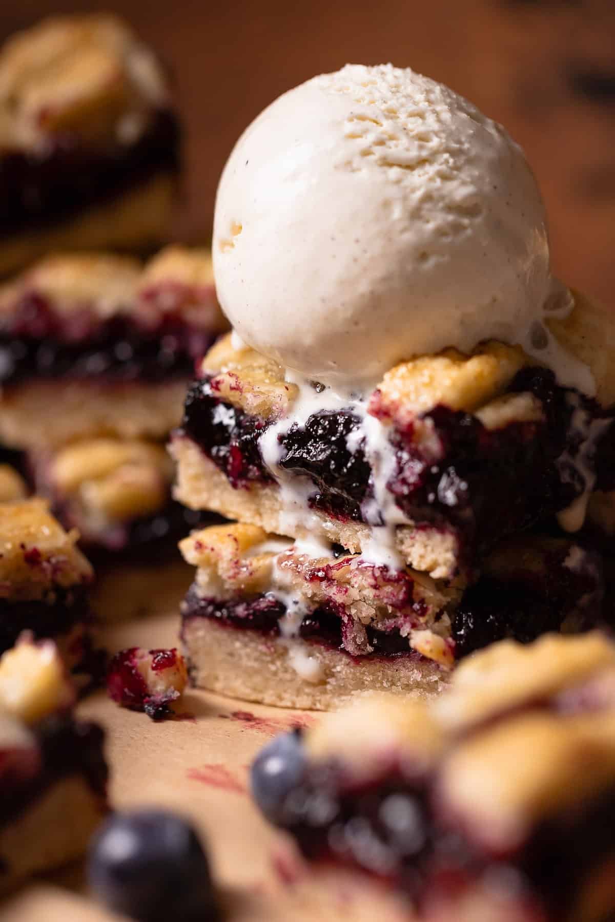 Two blueberry pie bars topped with a scoop of vanilla ice cream.
