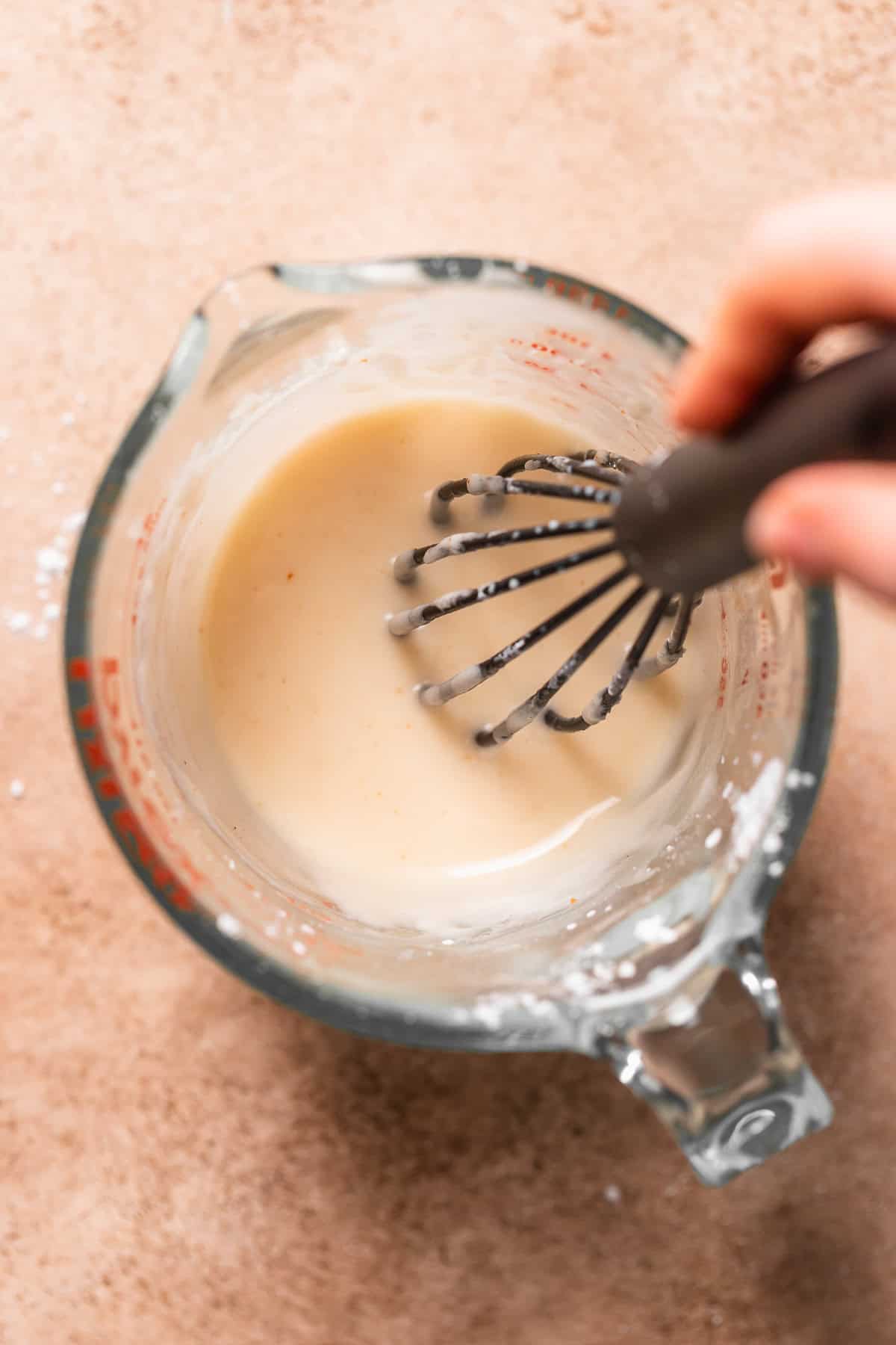 A hand whisking the brown butter glaze in a measuring glass.