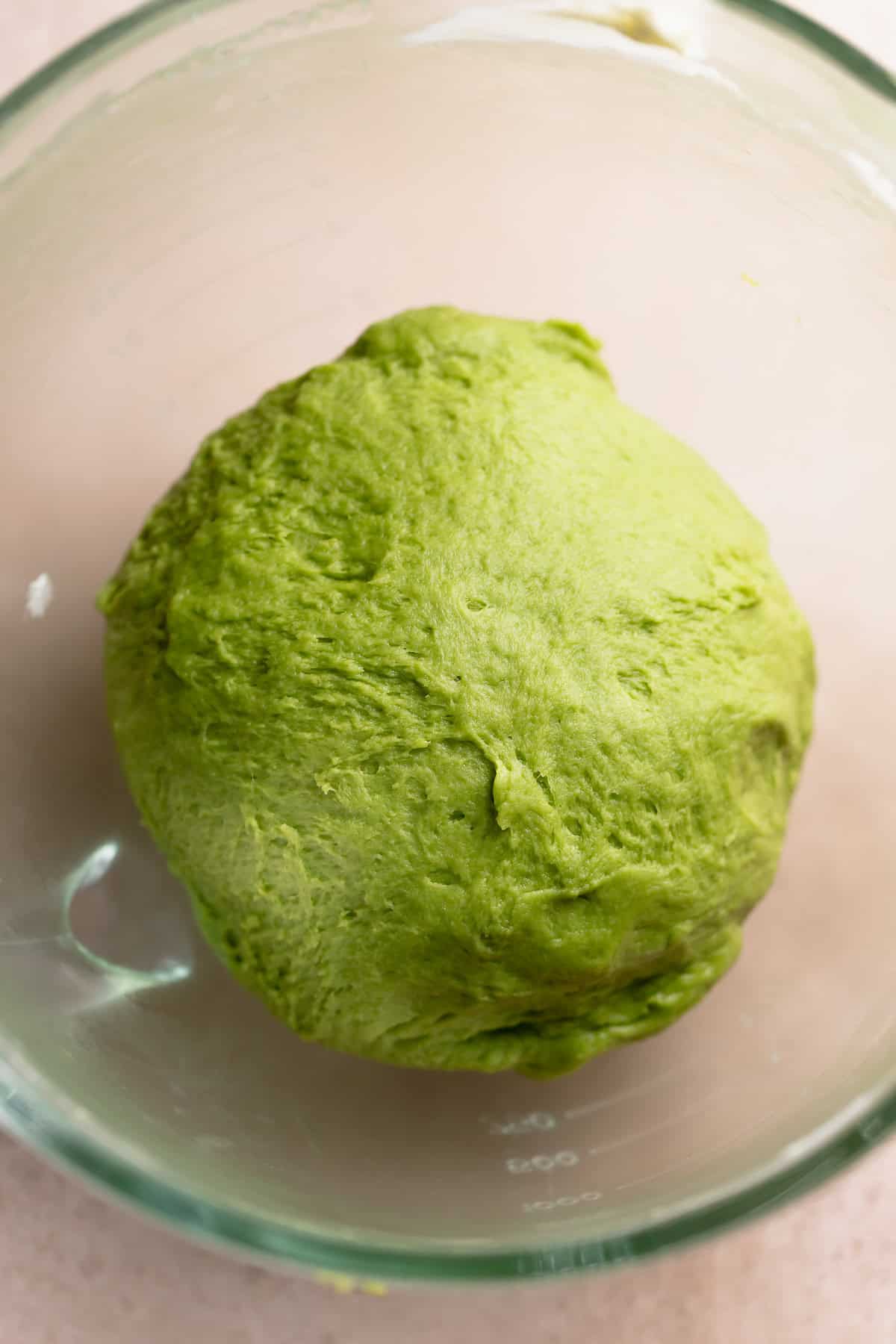 Matcha dough ball in a glass mixing bowl resting.