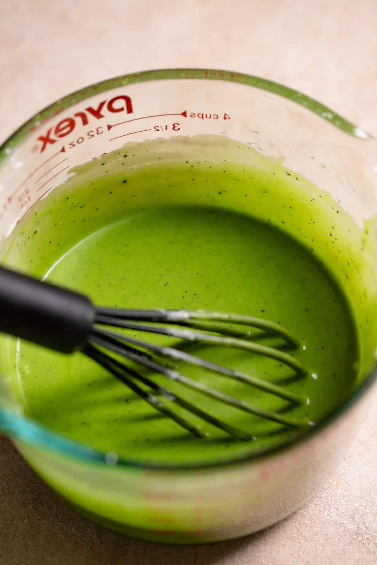 Matcha icing in a glass bowl with a whisk.