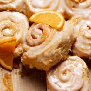Orange cinnamon rolls in a baking pan with fresh orange slices on top.