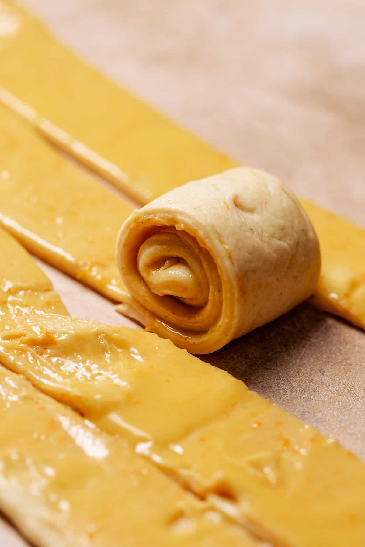A strip of orange dough being rolled up into a cinnamon roll.