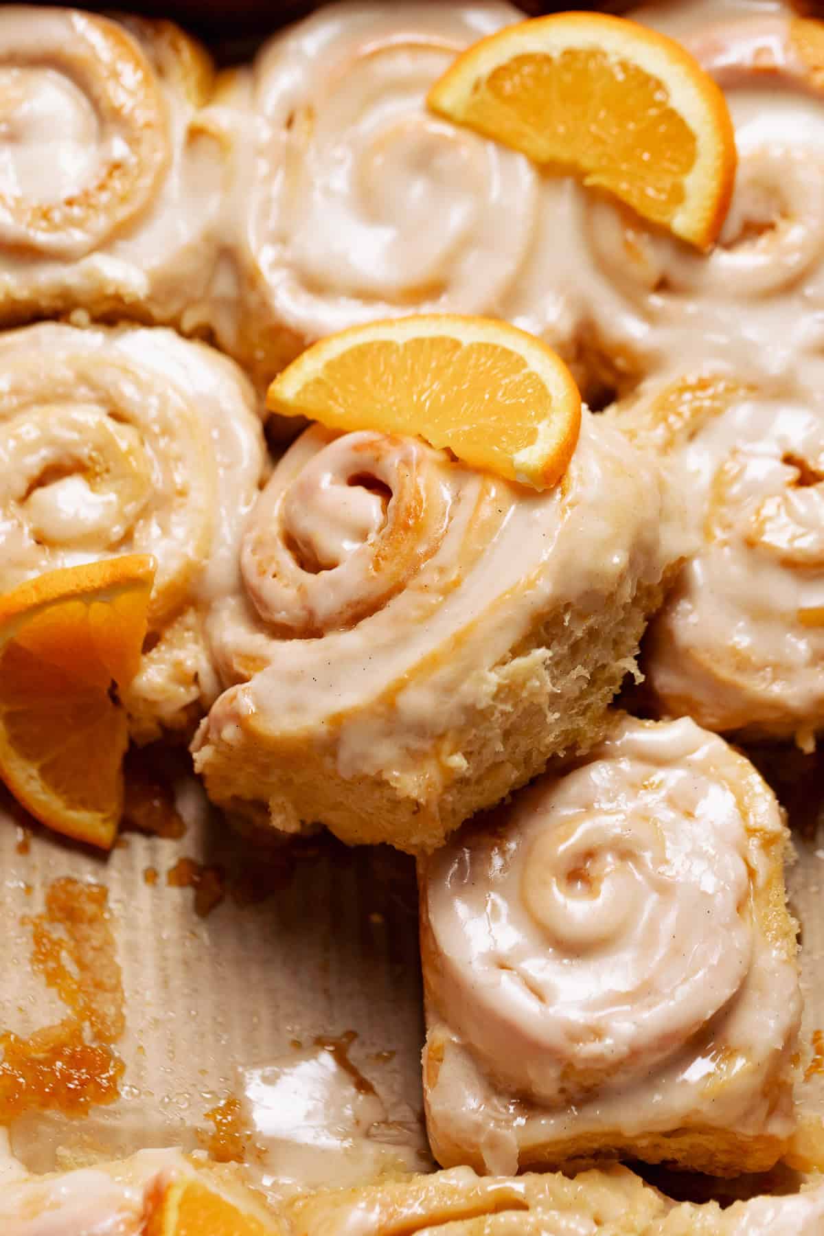 Orange cinnamon rolls in a baking pan topped with fresh oranges.