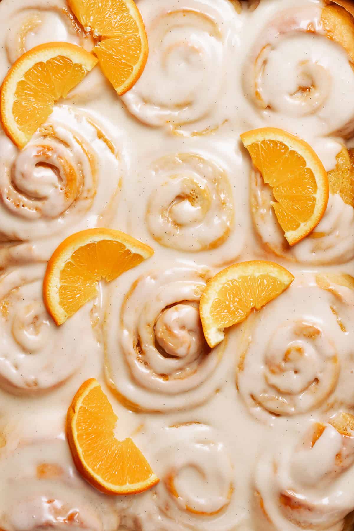 Orange cinnamon rolls covered in vanilla cream frosting and fresh orange slices.
