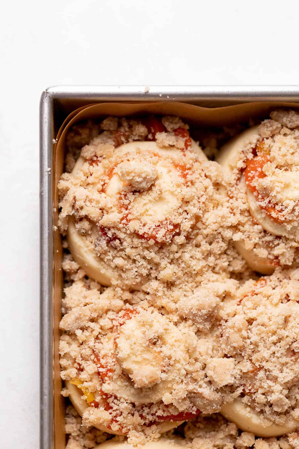 Peach cinnamon rolls with crumb topping in a baking pan right before baking.