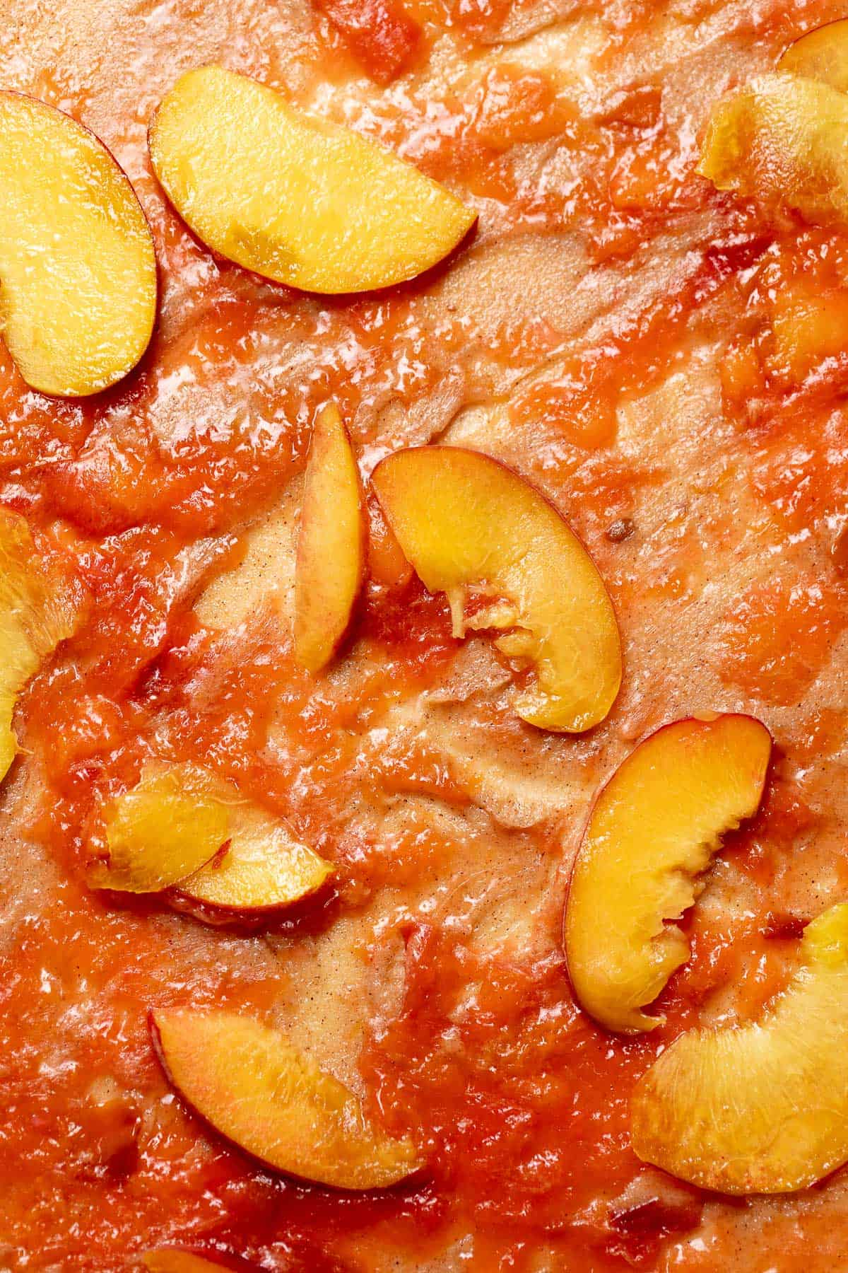 Cinnamon roll dough covered in peaches and peach jam.