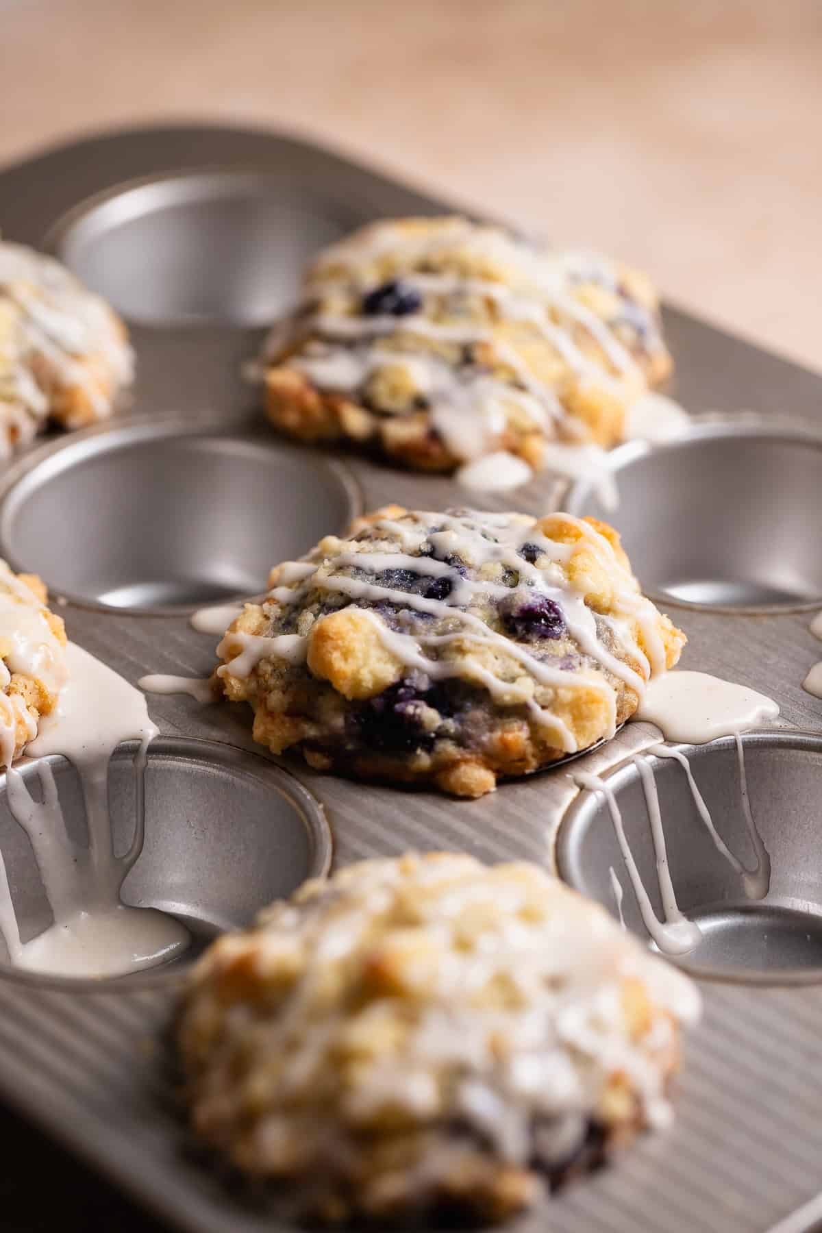 Muffins in a baking pan drizzled with vanilla glaze.
