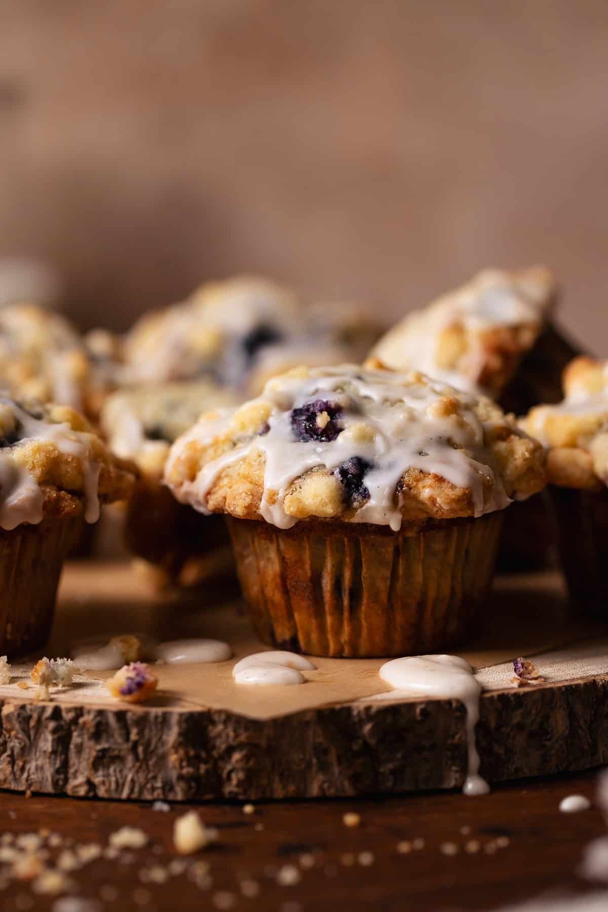 Blueberry muffins with crumb topping and vanilla glaze on a wooden platter.