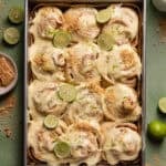 Key lime cinnamon rolls in a baking pan with key limes and graham crackers on top.