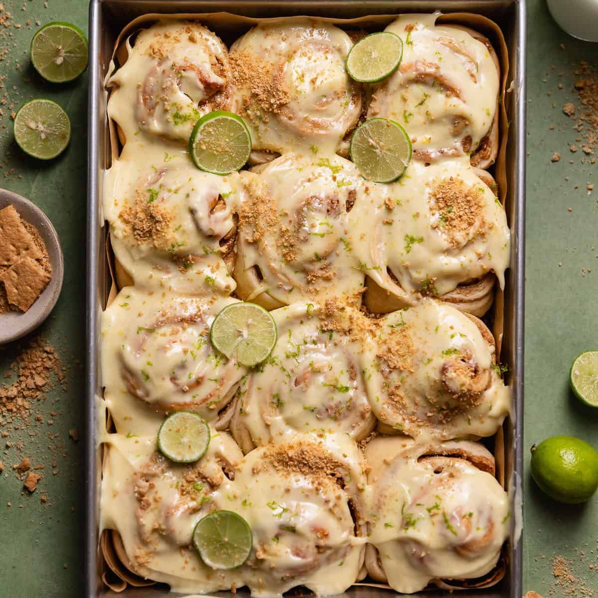 Key lime cinnamon rolls in a baking pan with key limes and graham crackers on top.