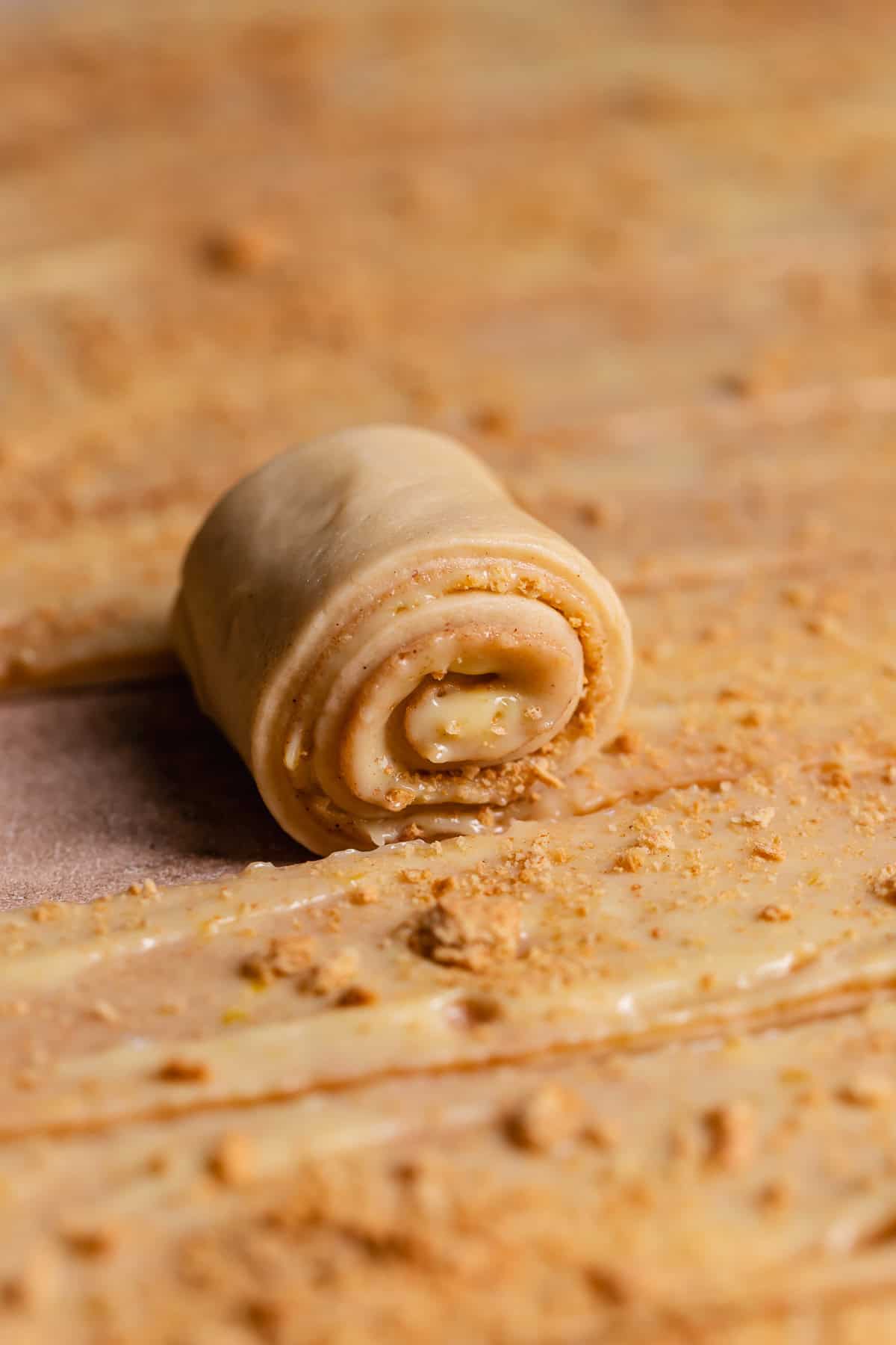 A strip of cinnamon roll dough being rolled up.