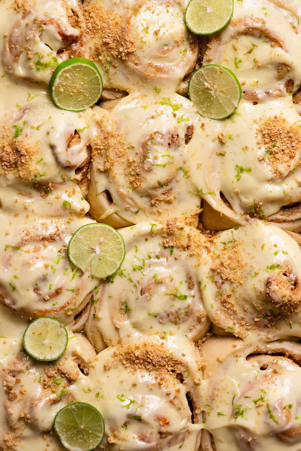 Key lime pie rolls with cream cheese frosting, key limes, and graham cracker crumbs on top.