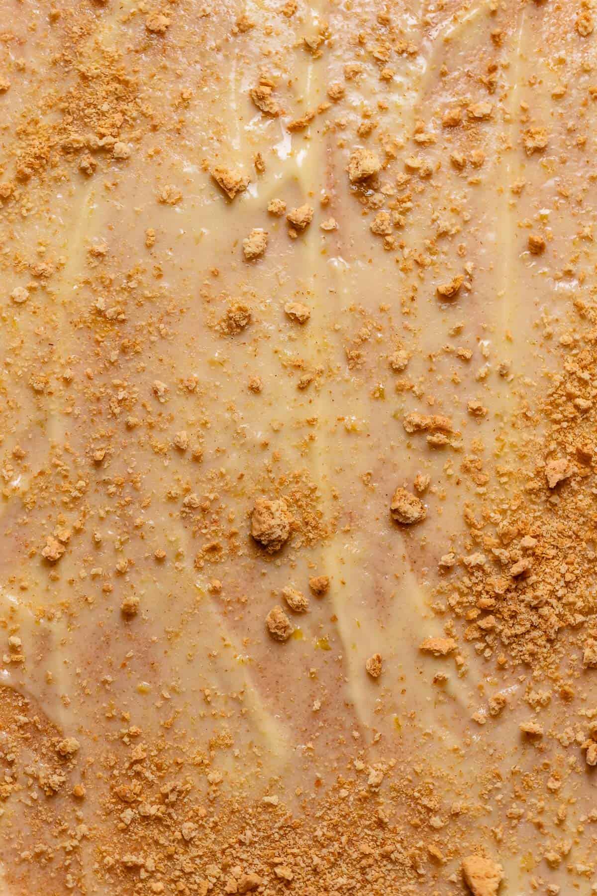 Cinnamon roll dough with key lime pie filling spread across it with graham crackers on top.
