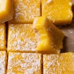 Lemon bars dusted with powdered sugar with one missing a bite.