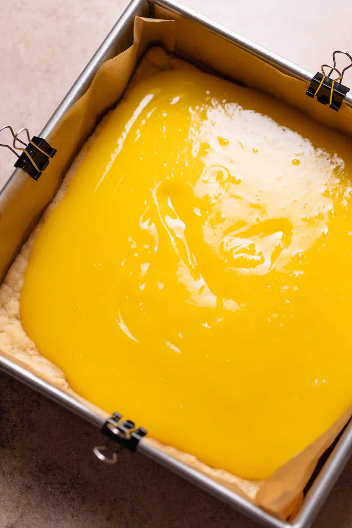 Lemon curd being spread over the top of the baked shortbread crust.