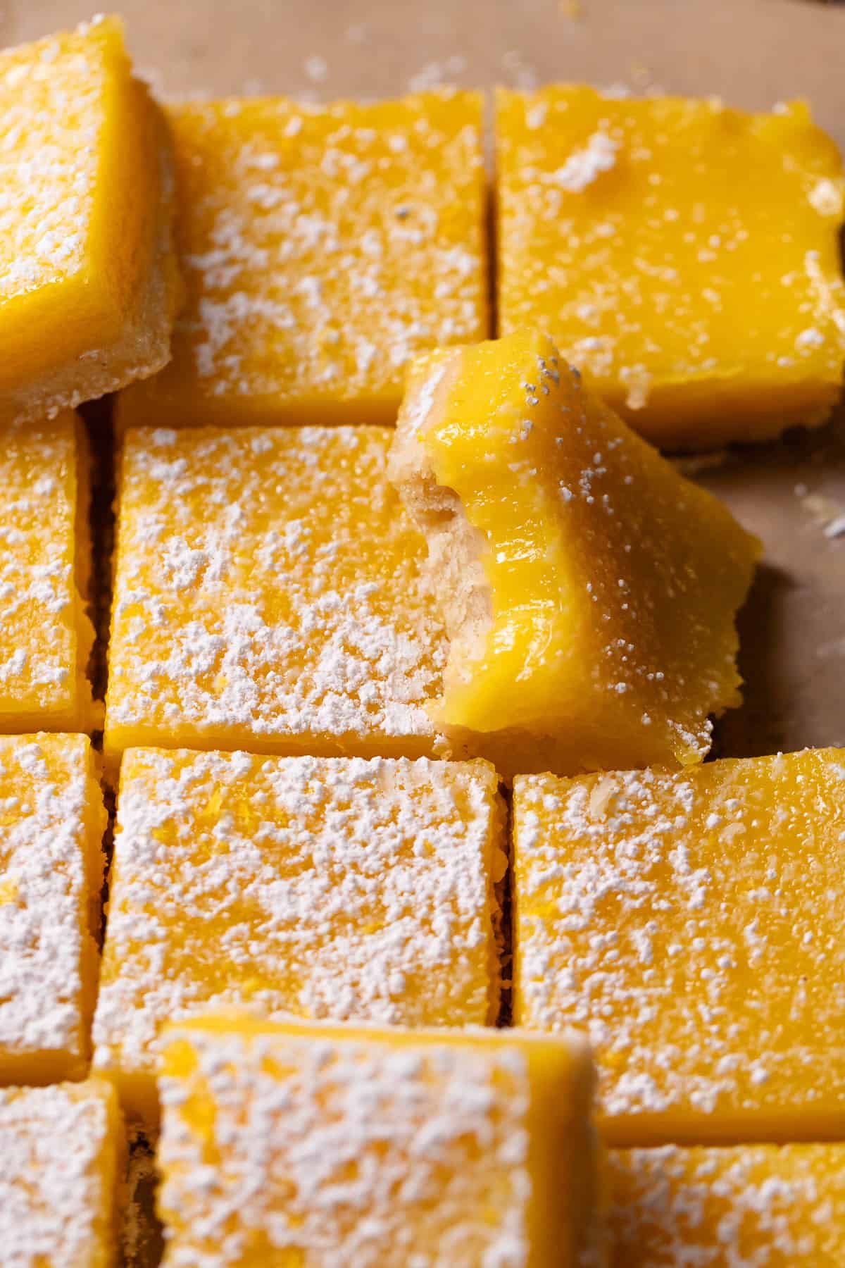 Lemon bars dusted with powdered sugar with one missing a bite.