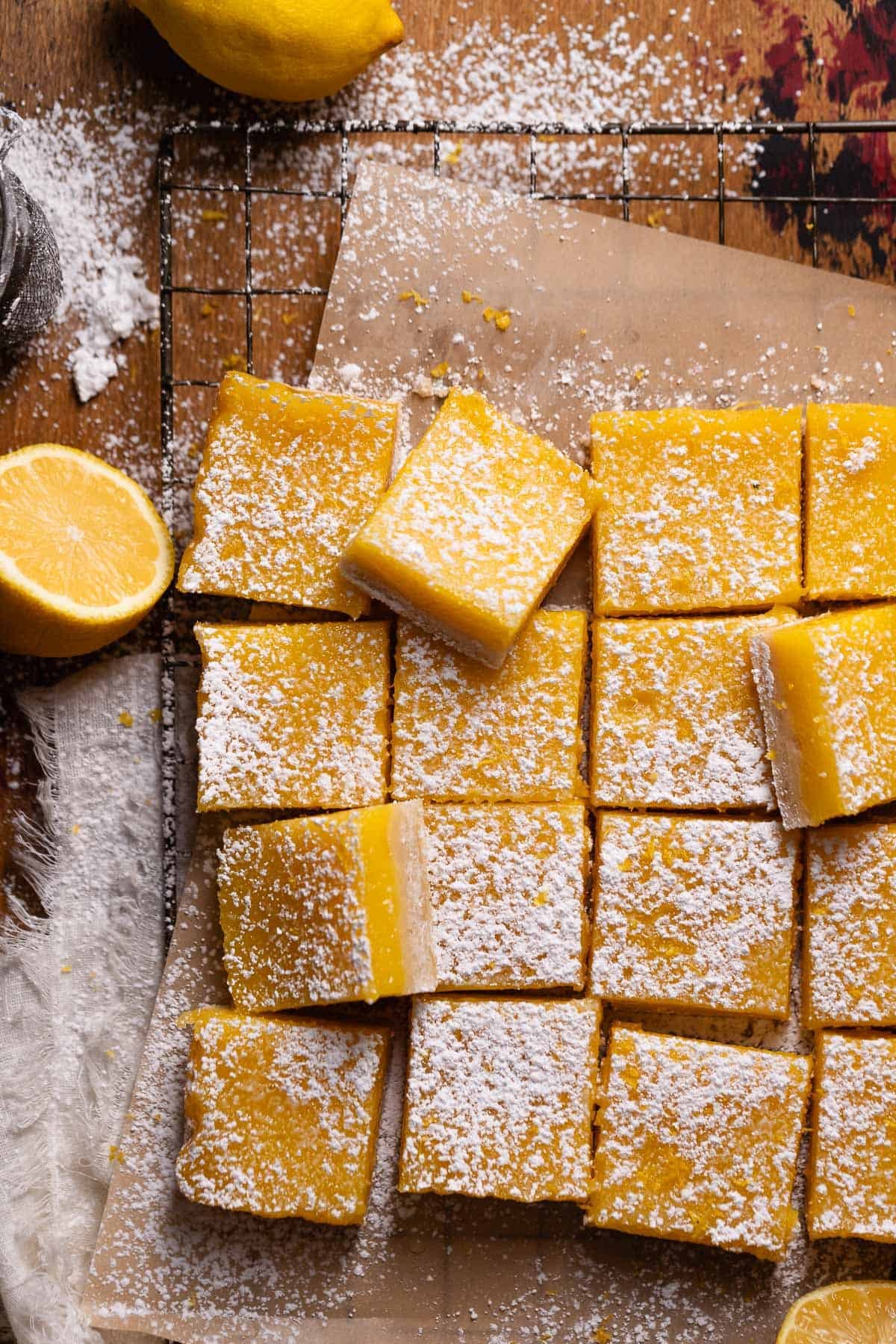 Lemon bars cut into squares and dusted with powdered sugar on brown parchment paper.