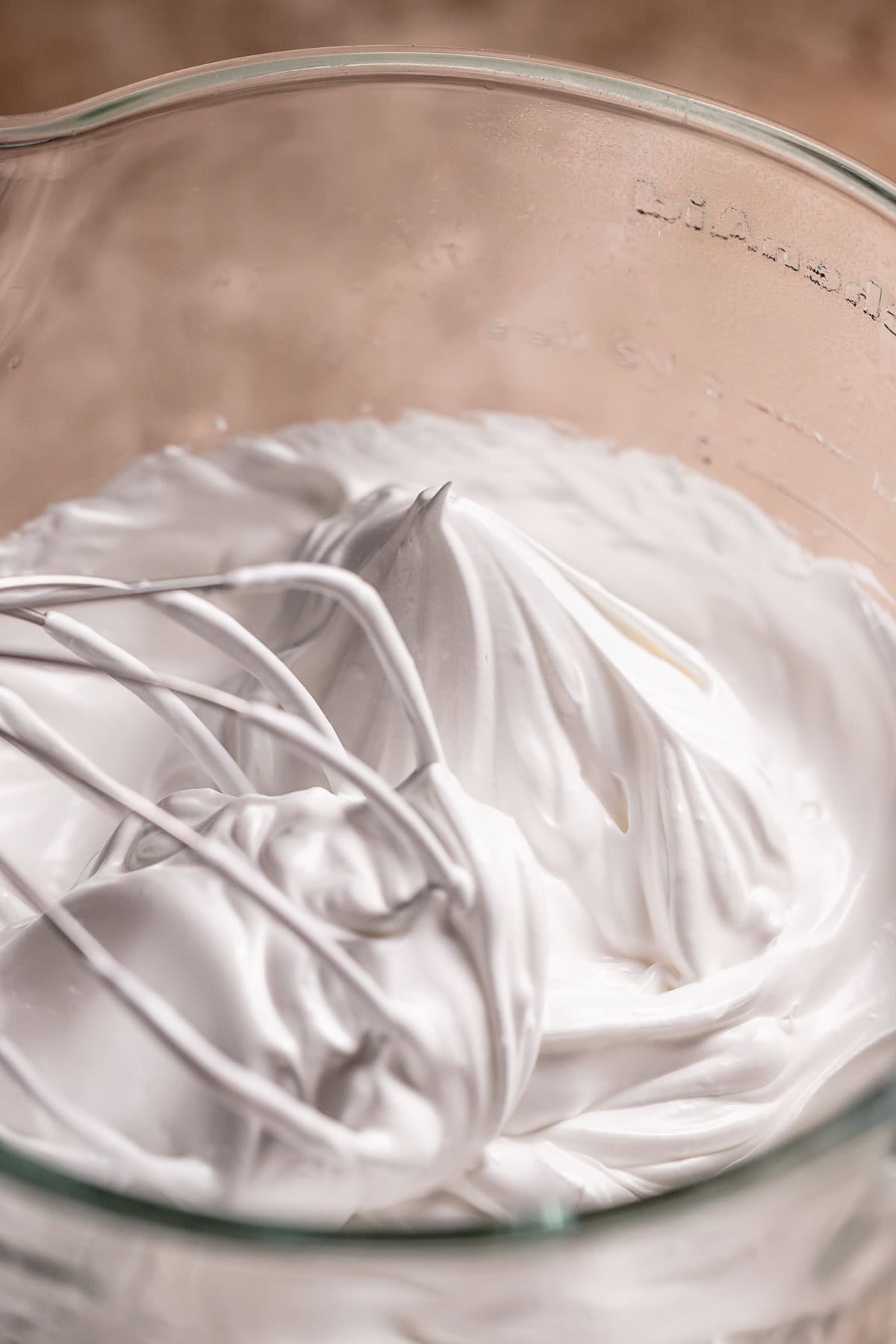 Italian meringue frosting with stiff peaks in a glass mixer bowl.