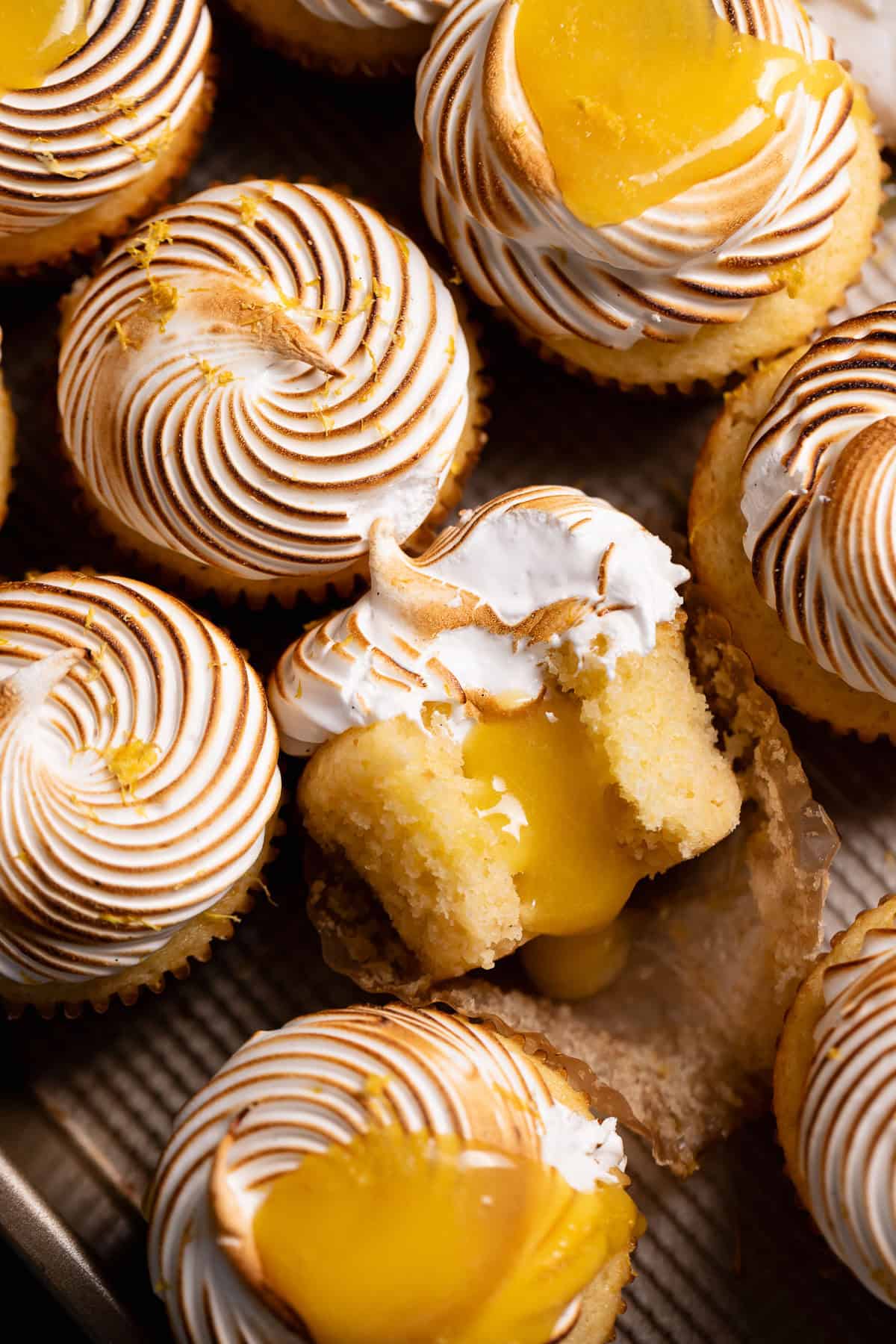 Lemon meringue pie cupcakes on a baking tray with the center one missing a bite to show the curd filling.