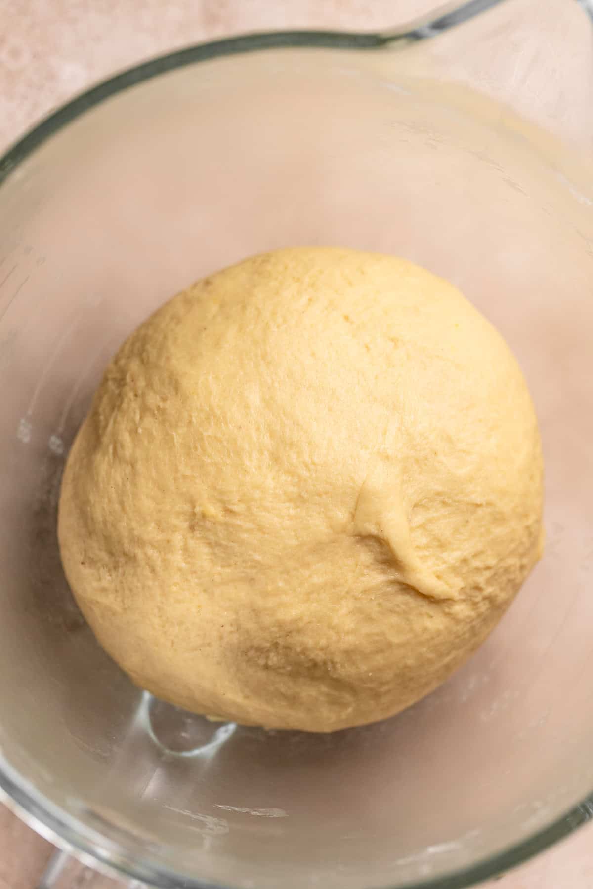A smooth dough ball resting in a glass mixing bowl.