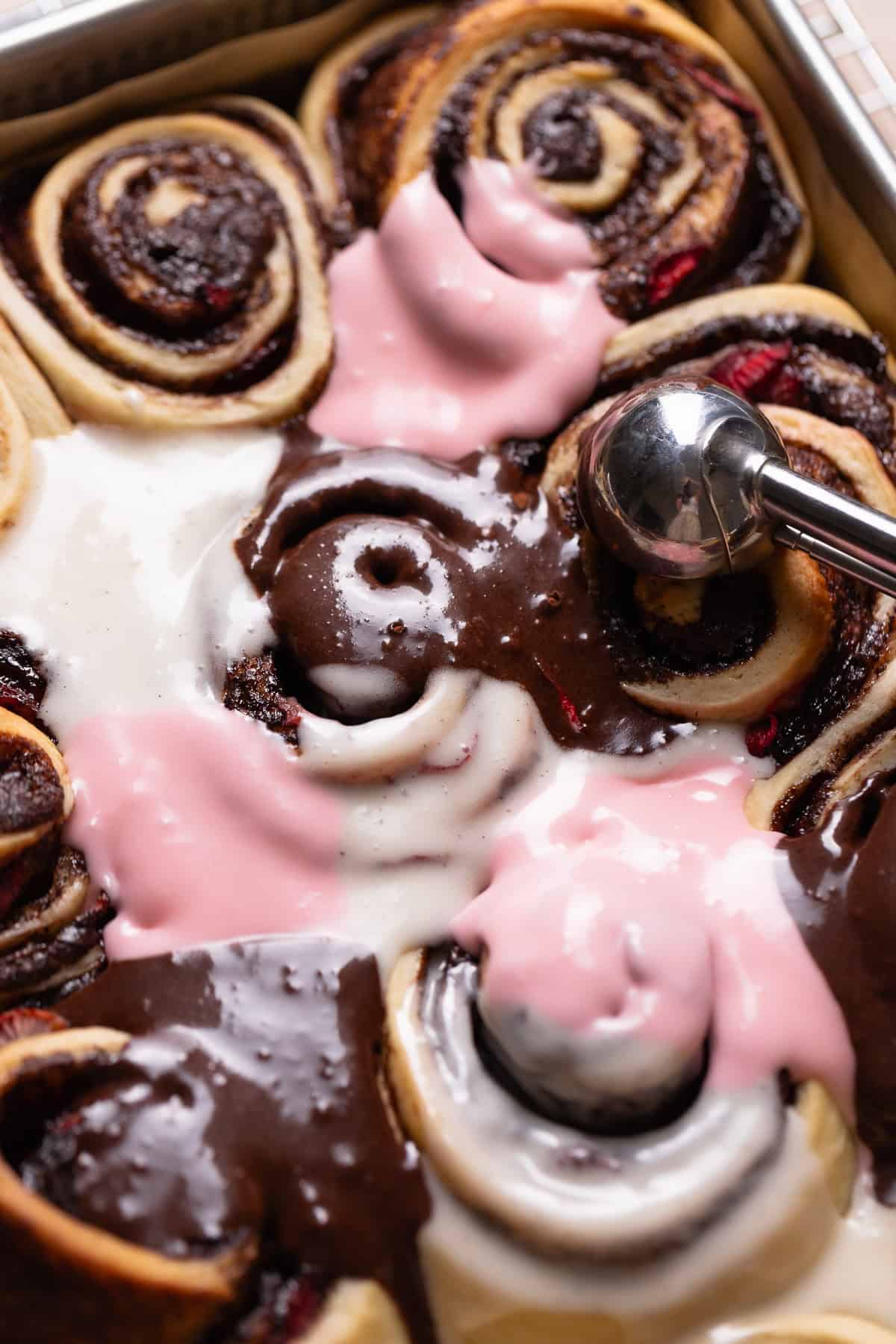 A scoop alternating the three icing colors on top of the baked cinnamon rolls.