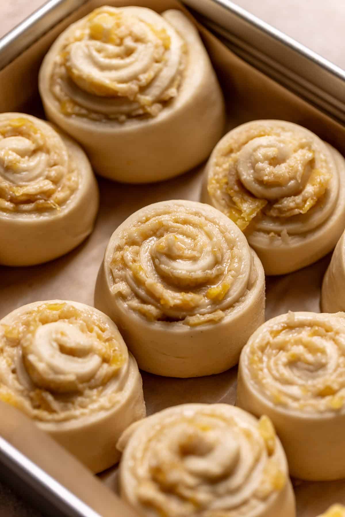 Pineapple coconut rolls in a baking pan barely touching before baking.