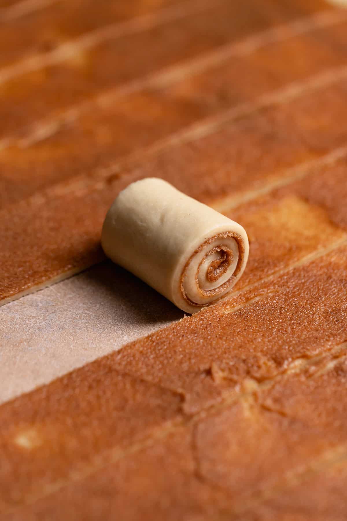 A cinnamon roll strip being rolled up.
