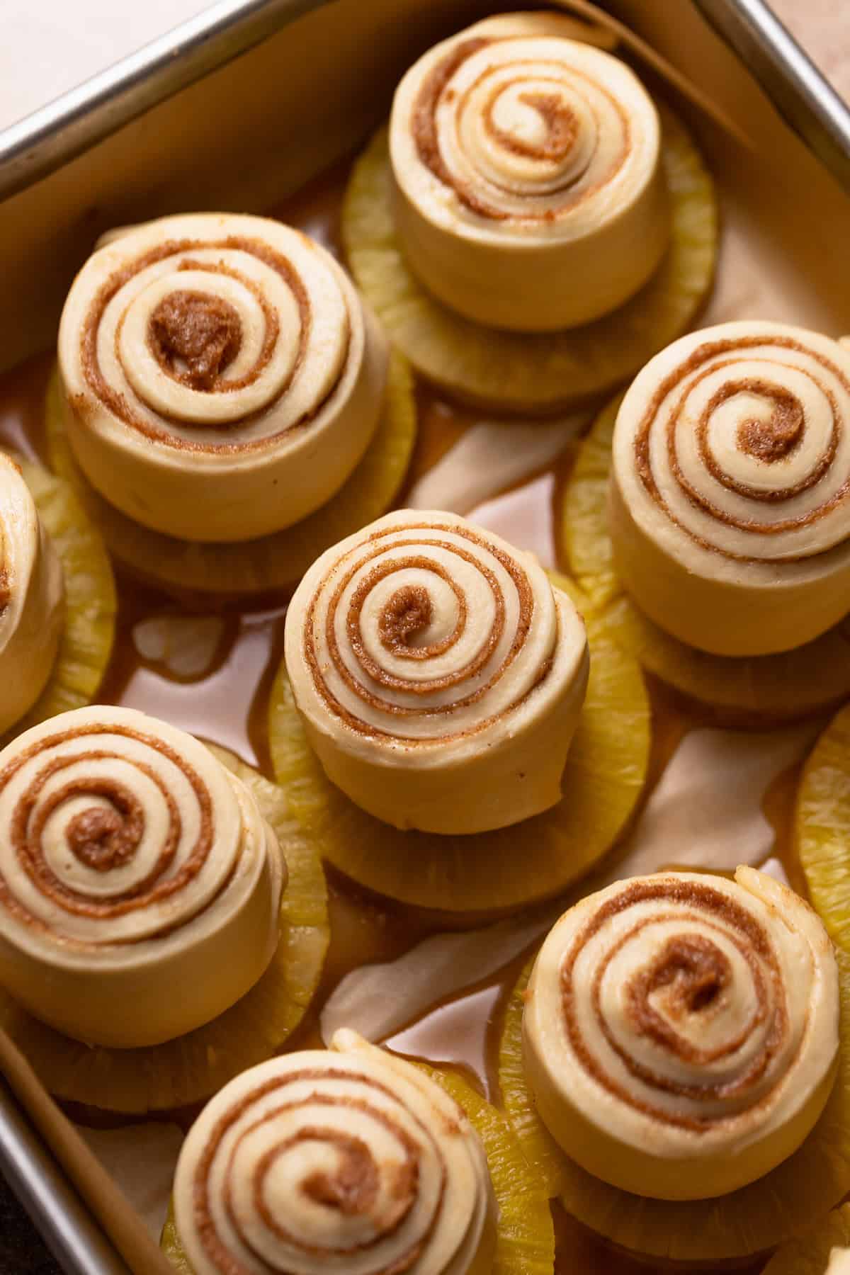 Cinnamon rolls sitting on top of the pineapple and caramel in a baking pan.