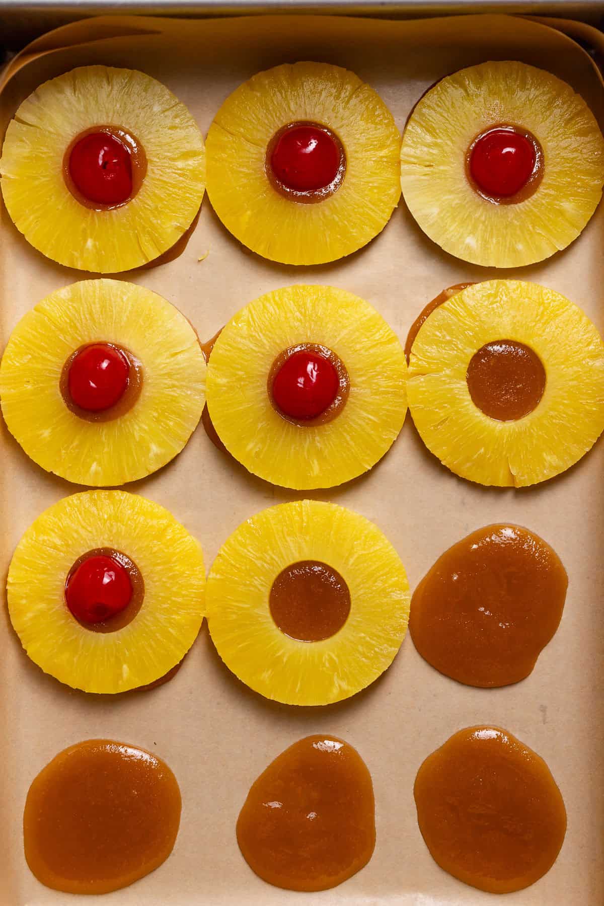 The bottom of a baking dish with the caramel, pineapple slices, and cherries being layered.
