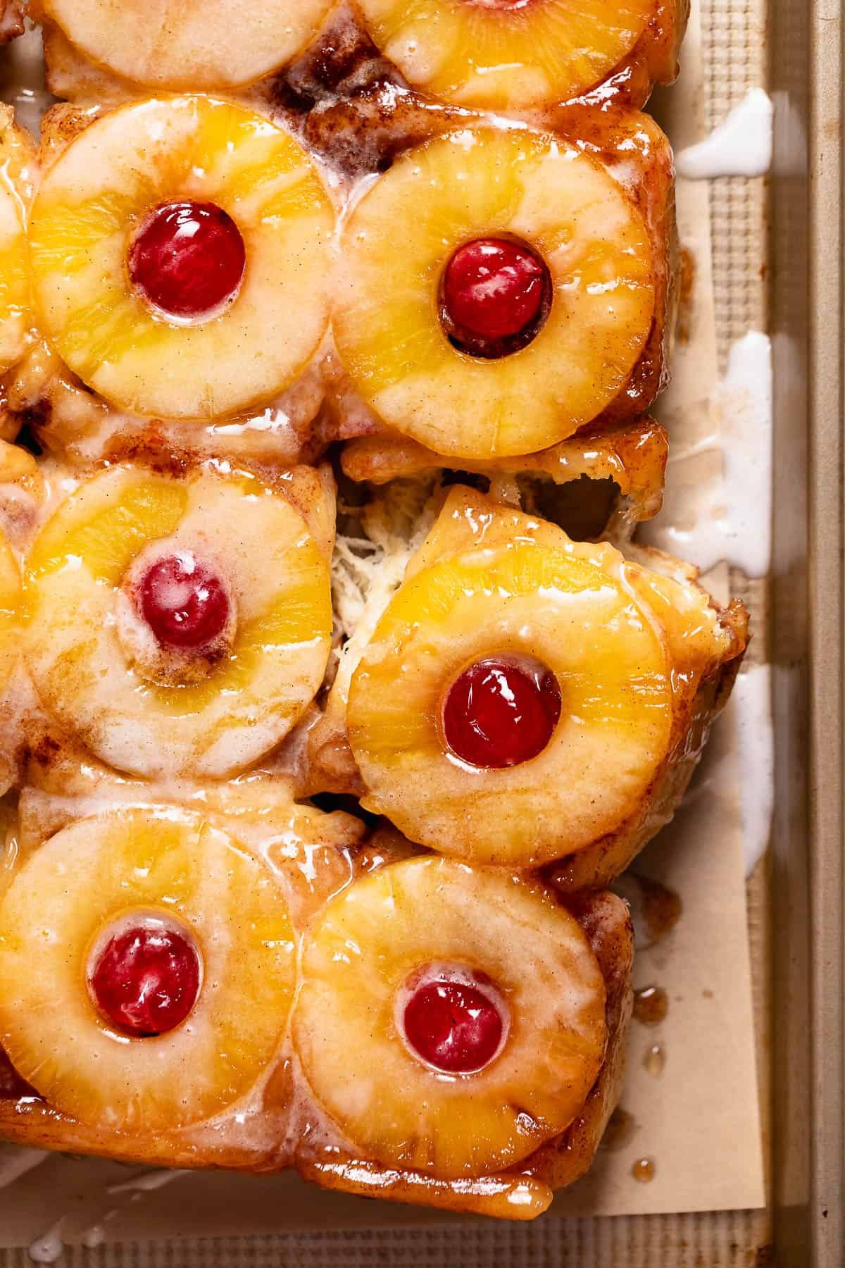 Pineapple upside down rolls on a baking pan drizzled with vanilla glaze.