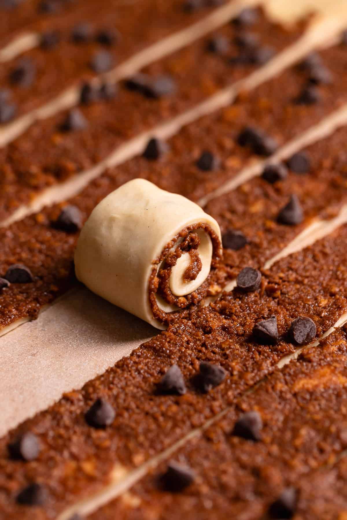 A strip of dough being rolled up into a cinnamon roll.