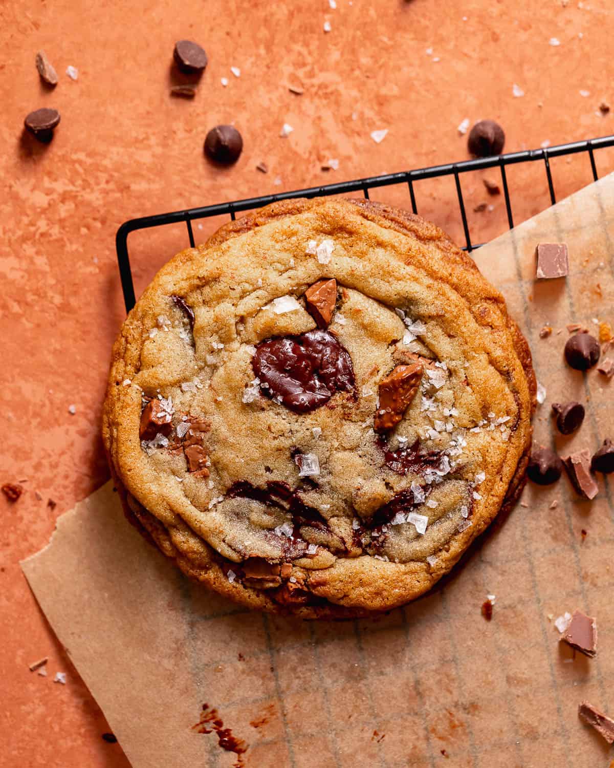 Chocolate chip cookie sprinkled with flaky sea salt on a wire rack.
