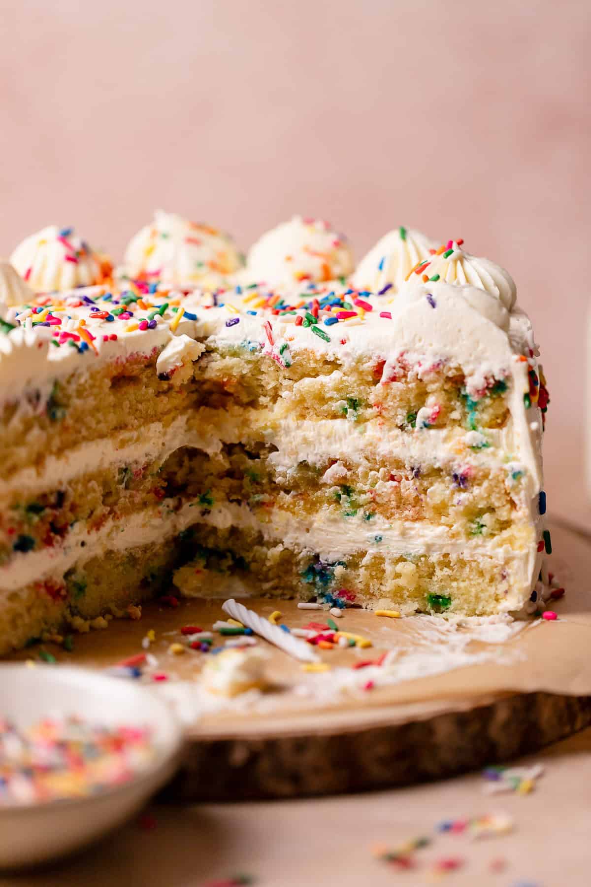 Funfetti cake with rainbow sprinkles on a cake stand missing slices.