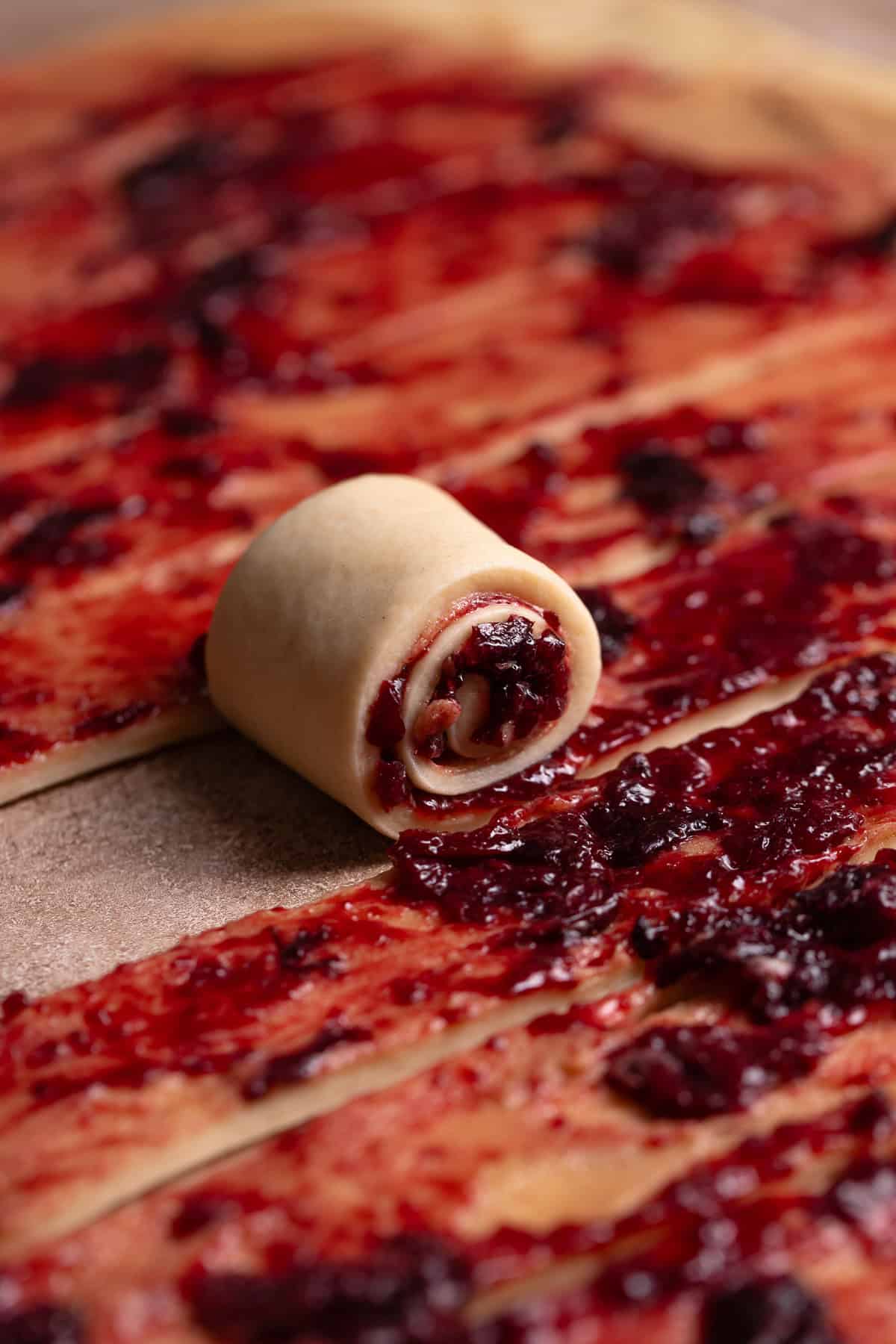 A strip of cherry cinnamon roll dough being rolled up into a roll.